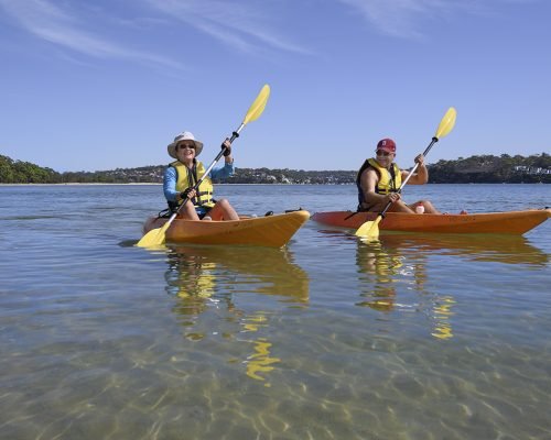 people on kayaks paddling along beach